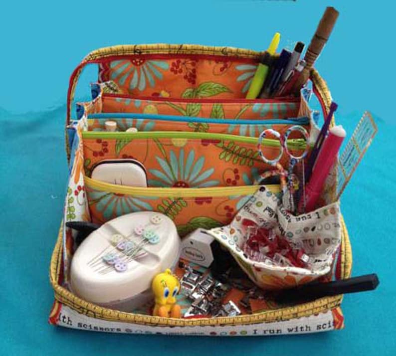 May include: A multi-colored fabric storage tote with multiple compartments. The tote is filled with sewing supplies, including scissors, needles, thread, and buttons. The tote has a yellow and white tape measure around the edge with the text "I run with scissors".