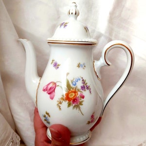 May include: White porcelain teapot with a floral design and gold trim. The teapot has a lid and a handle.
