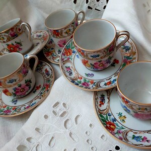 May include: Set of five white porcelain teacups and saucers with floral and gold accents. The cups and saucers feature a delicate floral pattern with gold trim.