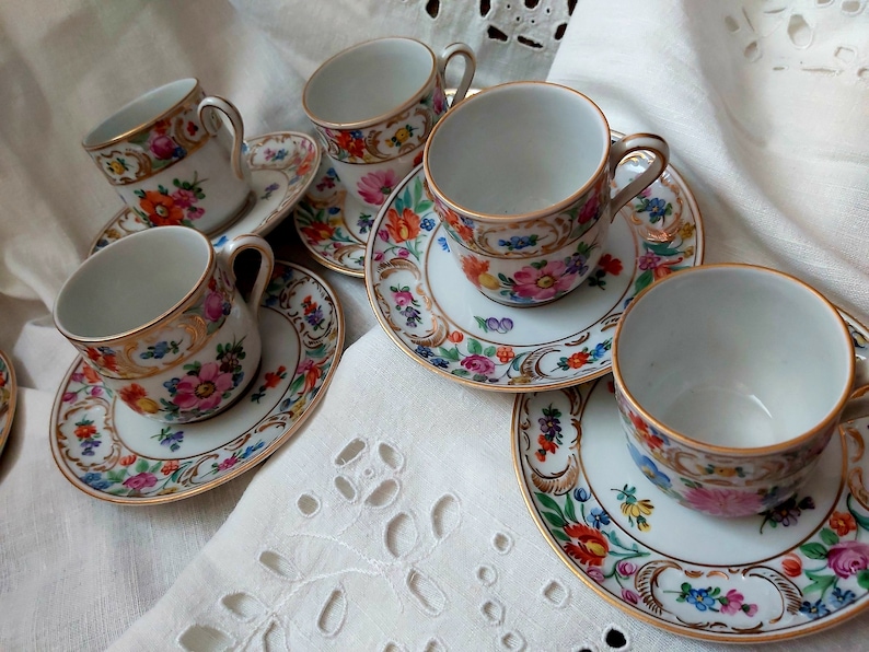 May include: Set of five white porcelain teacups and saucers with floral and gold accents. The cups and saucers feature a delicate floral pattern with gold trim.