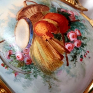 K&ouml;nnte beinhalten: Eine antike Porzellanvase mit handbemaltem Motiv eines Korbes, einer Trommel und Blumen. Die Vase ist mit goldenen Akzenten verziert und hat ein zartes Blumenmuster.