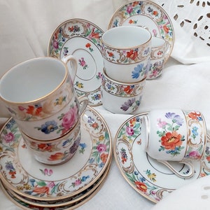 May include: Set of six vintage porcelain teacups and saucers with floral patterns in shades of pink, blue, yellow, and green. The cups and saucers have gold trim.