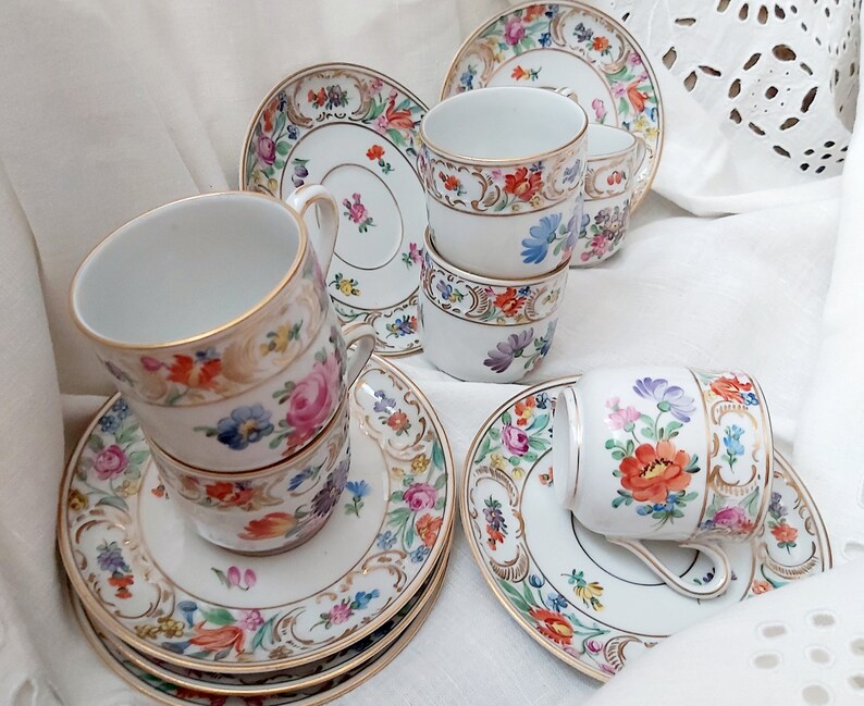 May include: Set of six vintage porcelain teacups and saucers with floral patterns in shades of pink, blue, yellow, and green. The cups and saucers have gold trim.