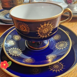 Puede incluir: Un juego de taza y platillo de porcelana azul profundo con un patrón repetitivo de estrellas doradas y bordes dorados. La taza tiene un interior blanco y un asa dorada, mientras que el platillo y el plato a juego muestran el mismo motivo.
