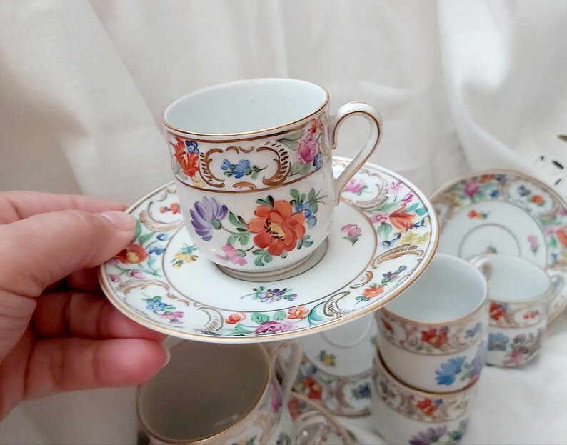 May include: A set of vintage porcelain teacups and saucers with floral patterns in shades of pink, blue, and yellow. The cups and saucers have gold trim and are decorated with delicate floral designs.