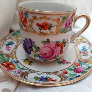 May include: A white porcelain teacup and saucer with a gold rim and floral pattern. The cup has a handle and the saucer has a scalloped edge.