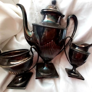 Puede incluir: Un juego de té de plata con tetera, jarra de crema y azucarero. El juego es de estilo tradicional con detalles ornamentados y un acabado oscuro envejecido.