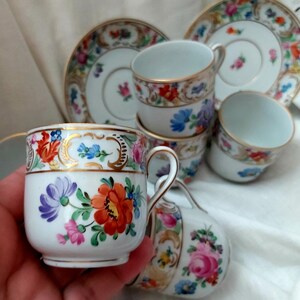 May include: Set of six vintage porcelain teacups and saucers with floral patterns and gold accents. The cups and saucers feature a delicate floral design with pink, blue, and yellow flowers. The gold accents add a touch of elegance to the design.