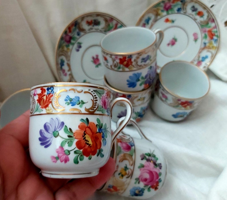 May include: Set of six vintage porcelain teacups and saucers with floral patterns and gold accents. The cups and saucers feature a delicate floral design with pink, blue, and yellow flowers. The gold accents add a touch of elegance to the design.