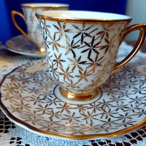 May include: A set of four white teacups and saucers with a gold floral pattern. The cups and saucers have a delicate, feminine design.
