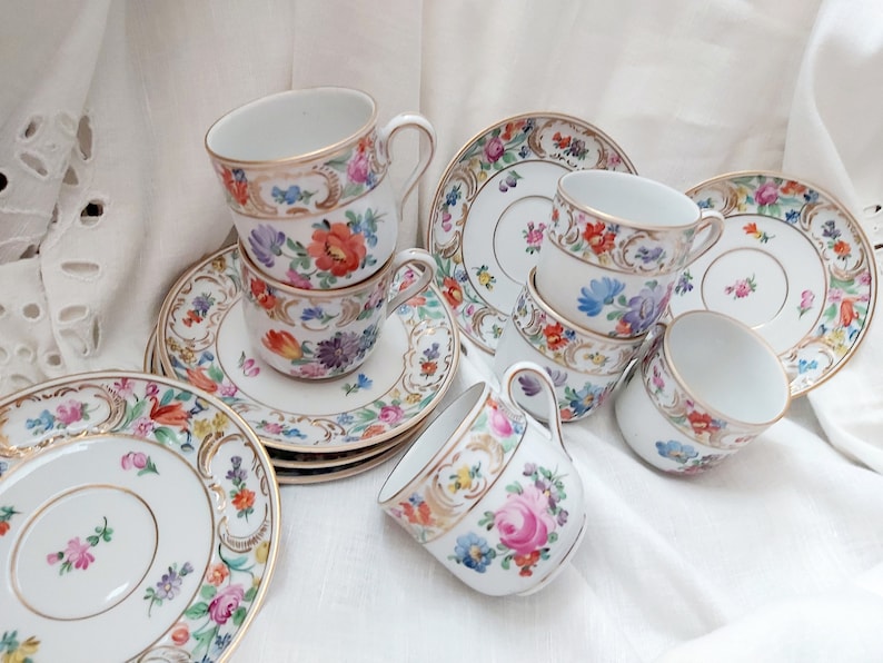 May include: A set of six vintage porcelain teacups and saucers with floral patterns in shades of pink, blue, yellow, and green. The cups and saucers have gold trim and are in excellent condition.
