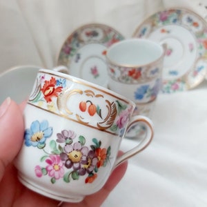 May include: A set of delicate porcelain teacups and saucers with floral patterns in shades of pink, blue, yellow, and green. The cups have gold trim and a delicate floral design.
