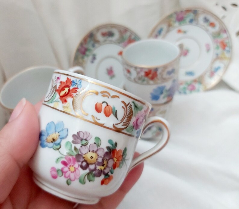 May include: A set of delicate porcelain teacups and saucers with floral patterns in shades of pink, blue, yellow, and green. The cups have gold trim and a delicate floral design.