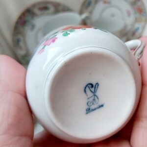 May include: A white porcelain teacup with a floral pattern and a blue and white mark on the bottom that reads "Dresden".