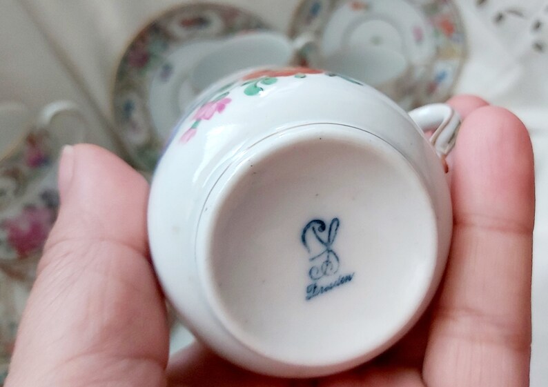 May include: A white porcelain teacup with a floral pattern and a blue and white mark on the bottom that reads "Dresden".