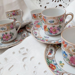 May include: Set of four floral teacups and saucers with gold trim. The cups and saucers feature a delicate floral pattern with pink, blue, and yellow flowers.