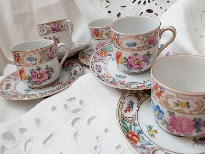 May include: Set of four floral teacups and saucers with gold trim. The cups and saucers feature a delicate floral pattern with pink, blue, and yellow flowers.