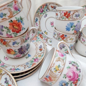 May include: A set of vintage teacups and saucers with floral patterns in shades of pink, blue, yellow, and red. The cups and saucers have gold trim and intricate floral designs.