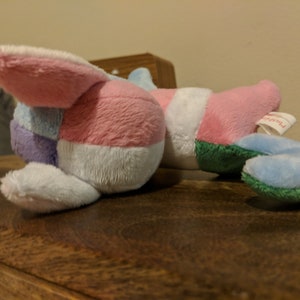 K&ouml;nnte beinhalten: Ein Pl&uuml;schtier mit Patchwork-Design in Rosa, Blau, Wei&szlig; und Gr&uuml;n. Das Spielzeug hat ein langes, schlaffes Ohr und ein Etikett mit der Aufschrift "Plushville".