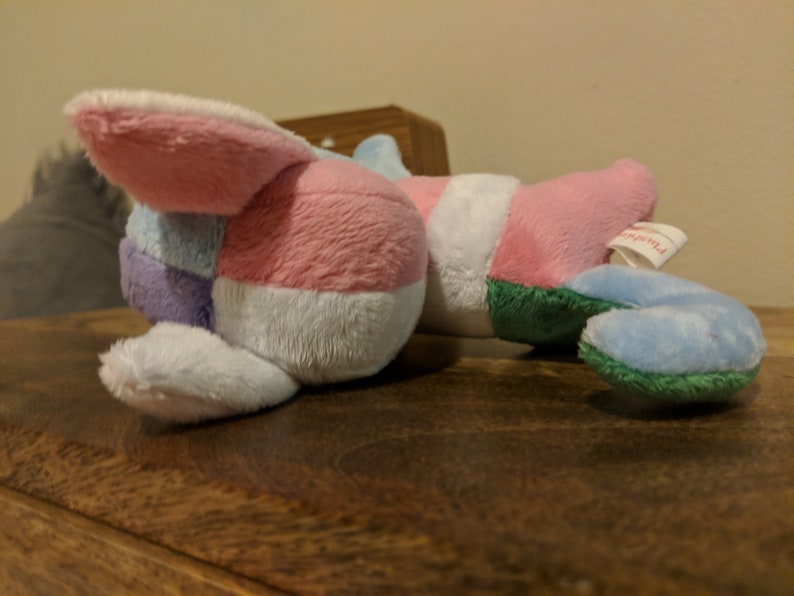 K&ouml;nnte beinhalten: Ein Pl&uuml;schtier mit Patchwork-Design in Rosa, Blau, Wei&szlig; und Gr&uuml;n. Das Spielzeug hat ein langes, schlaffes Ohr und ein Etikett mit der Aufschrift "Plushville".