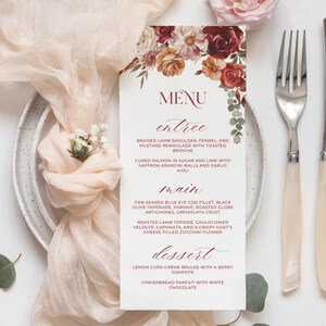 May include: A wedding menu card with floral accents, featuring a menu with entree, main, and dessert options. The card is placed on a plate with a fork and knife, alongside decorative flowers and fabric.