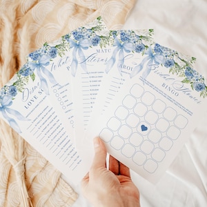 Könnte beinhalten: Eine Sammlung von Spielkarten für eine Brautparty mit floralen und Schleifen-Designs. Die Karten zeigen blaue Aquarellblumen und -schleifen mit Text in eleganten Schriftarten. Spiele sind Disney Love Song, Match the Literary und Bridal Shower Bingo.