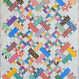 May include: A colorful quilt with a white background and a criss-cross pattern. The quilt is made of various fabrics with floral and geometric designs in shades of red, pink, blue, green, yellow, and purple.