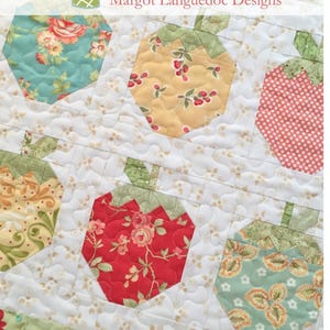May include: A quilted fabric with a strawberry pattern. The strawberries are in various colors and patterns, including red floral, yellow with berries, and teal floral. The text "Strawberry Social Mini" is at the bottom.