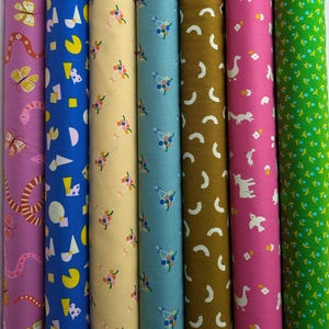 May include: A collection of rolled fabric bolts in various colors and patterns. Designs include butterflies, snakes, geometric shapes, floral arrangements, crescent moons, and animals. Colors include purple, blue, yellow, teal, brown, pink, and green.