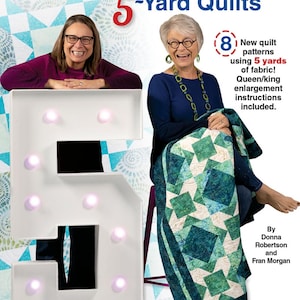 May include: Two women are sitting in front of a large white number 5 with light bulbs. The woman on the left is wearing a purple shirt and the woman on the right is wearing a blue shirt. The woman on the right is holding a blue and green quilt. The text "Fabulous 5-Yard Quilts" is at the top of the image. The text "8 New quilt patterns using 5 yards of fabric! Queen/king enlargement instructions included." is on the right side of the image. The text "By Donna Robertson and Fran Morgan" is at the bottom right of the image.