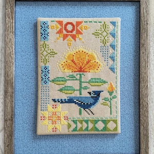 Peut inclure: Motif de point de croix intitulé "Seasonal Courier: Blue Jay's Summer" dans un cadre en bois. Le motif représente un geai bleu, une grande fleur jaune et des éléments géométriques et floraux de différentes couleurs. Le texte "Robin Pickens Cross Stitch Patterns" est en bas.