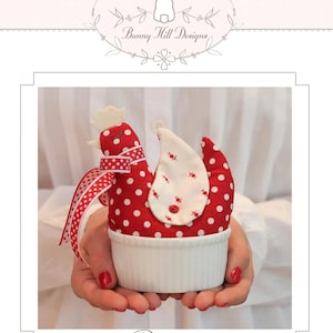 May include: A handmade red and white polka dot chicken-shaped item with a white base. The chicken has a white comb, a red and white ribbon, and a white wing with red accents. The word "Rosie" is at the bottom.