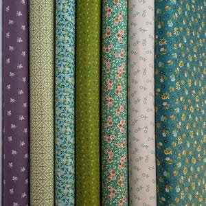 May include: A collection of rolled fabric bolts in various colors and patterns. The fabrics include floral, geometric, and leaf designs in shades of purple, green, and teal. The fabrics are tightly rolled, showcasing the variety of textures and prints.