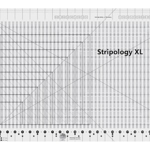 May include: A clear, rectangular quilting ruler with a grid pattern and the text "Stripology XL" printed on it. The ruler features various angled lines and measurement markings in inches, designed for precise fabric cutting and quilting projects.