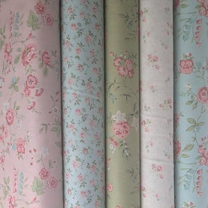 May include: A collection of fabric rolls featuring floral patterns. The fabrics display a variety of colors, including pink, blue, and green, with delicate rose and leaf designs. The rolls are tightly wound, showcasing the repeating patterns.