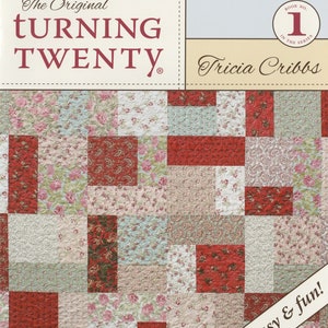 May include: The Original Turning Twenty quilt pattern book by Tricia Cribbs. The book cover features a quilt block design with red, pink, and green floral fabric squares. The text on the cover reads "The Original Turning Twenty" and "Fast, easy & fun!"