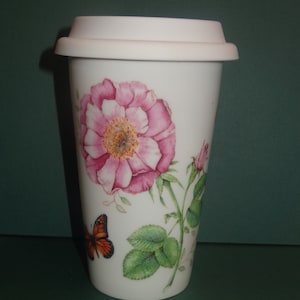 May include: White ceramic travel mug with a pink rose and green leaves design. A butterfly with orange and black wings is on the side of the mug.