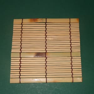 May include: A natural bamboo sushi rolling mat with brown string accents. The mat is made of thin strips of bamboo woven together.