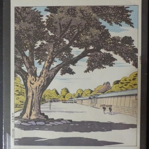 Pu&ograve; includere: Una stampa xilografica giapponese incorniciata raffigurante un grande albero con una chioma tentacolare, che proietta un'ombra su un sentiero. La scena comprende un lungo muro, edifici e figure, il tutto reso in toni tenui.