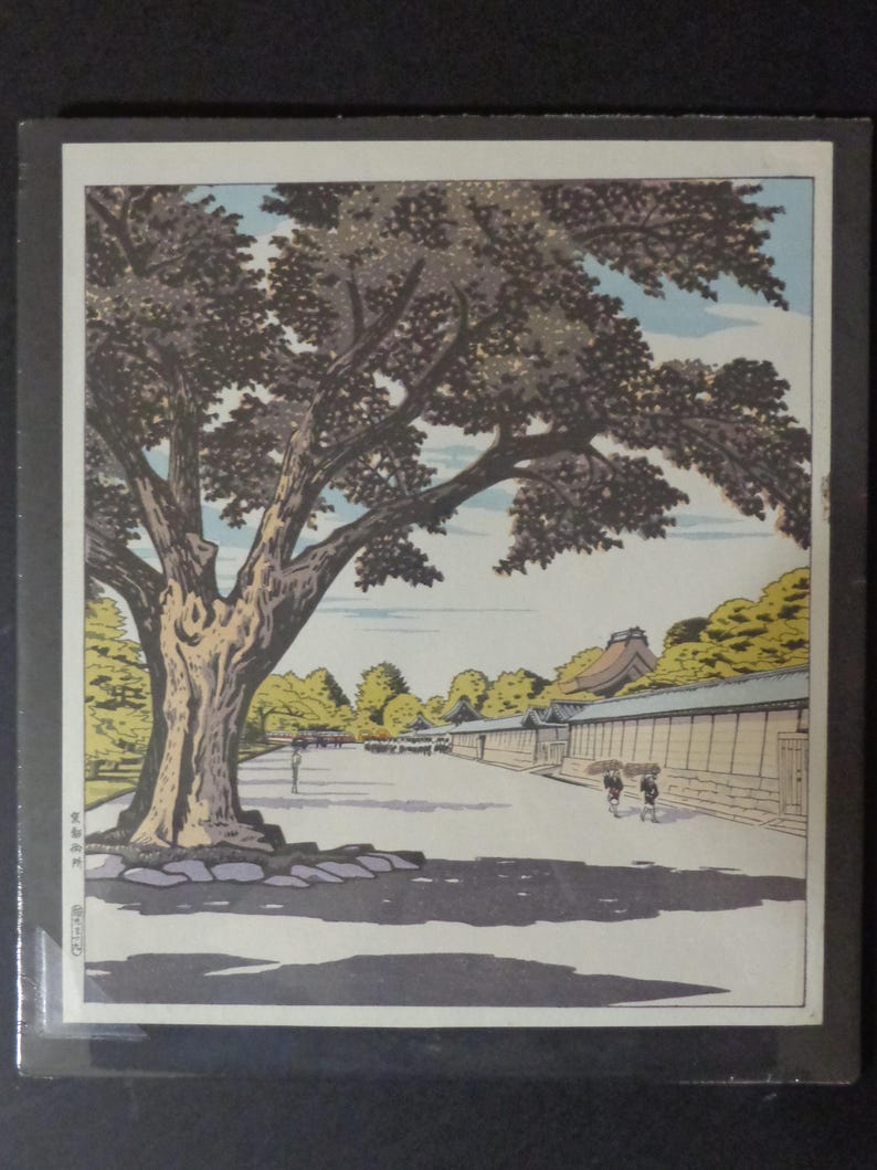 Pu&ograve; includere: Una stampa xilografica giapponese incorniciata raffigurante un grande albero con una chioma tentacolare, che proietta un'ombra su un sentiero. La scena comprende un lungo muro, edifici e figure, il tutto reso in toni tenui.
