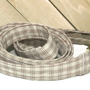 May include: A beige and brown plaid dog leash with a gold metal clasp.