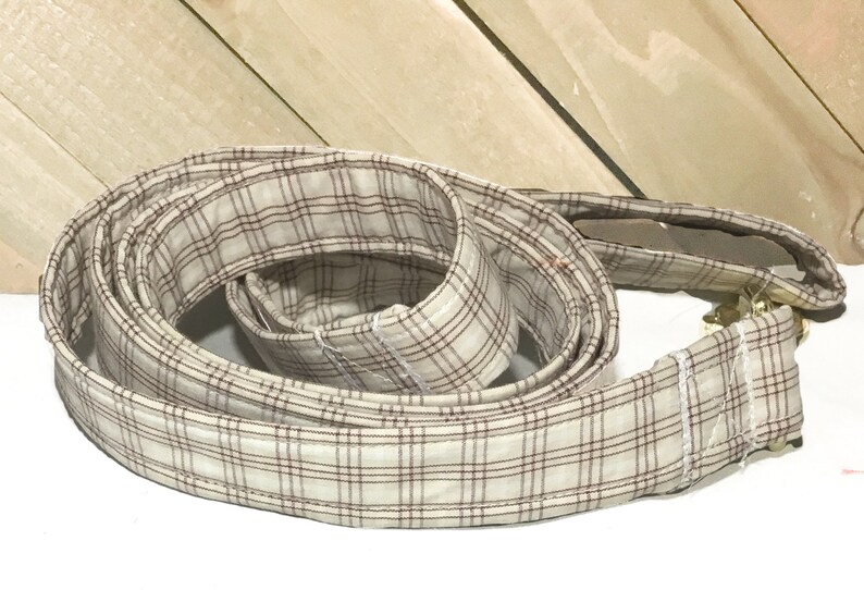 May include: A beige and brown plaid dog leash with a gold metal clasp.