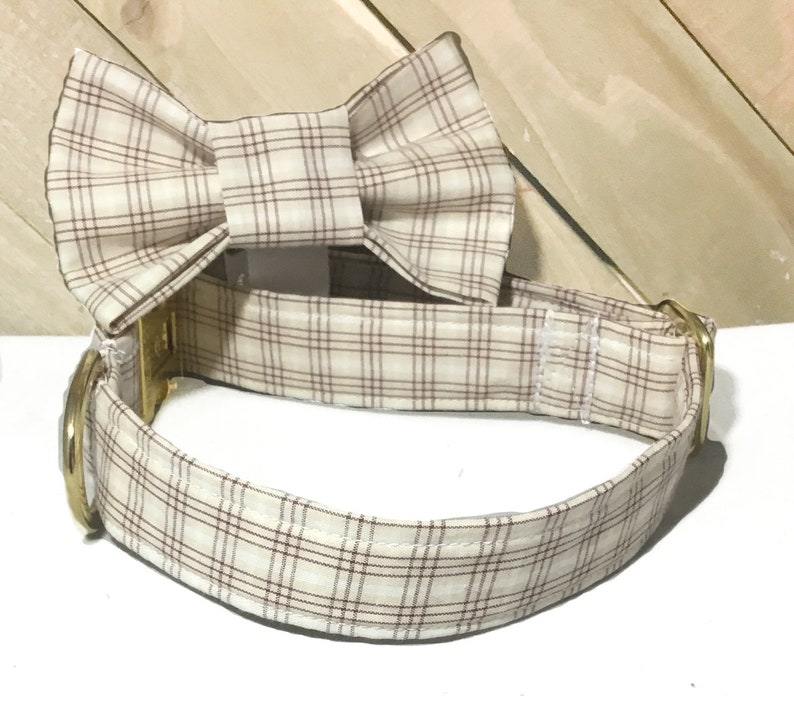 May include: A beige and brown plaid dog collar with a matching bow tie. The collar has a gold metal buckle.