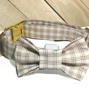 May include: A beige and brown plaid dog collar with a gold buckle and a matching bow tie.