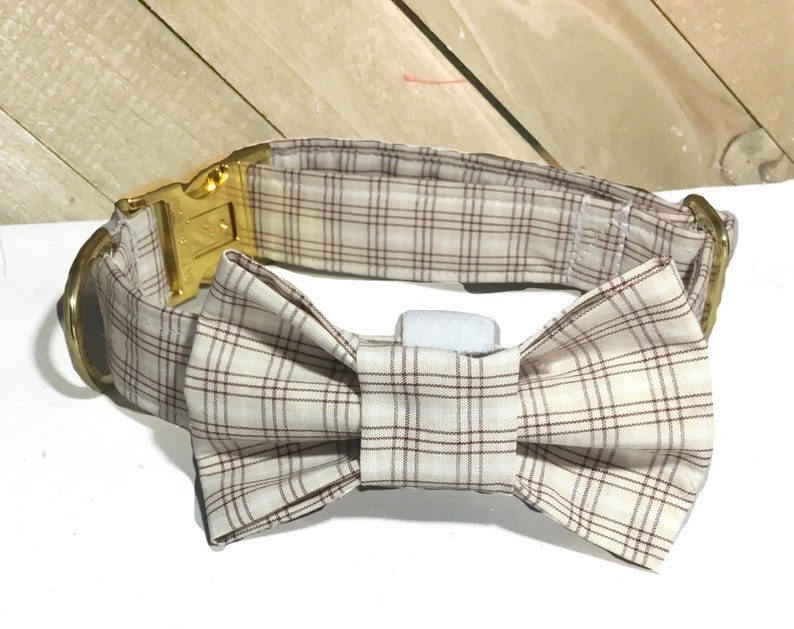 May include: A beige and brown plaid dog collar with a gold buckle and a matching bow tie.