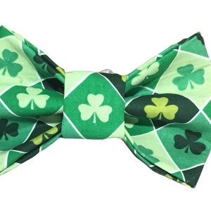 May include: Green bow tie with a shamrock pattern. The bow tie is made of fabric and has a checkered pattern with shamrocks in different shades of green.