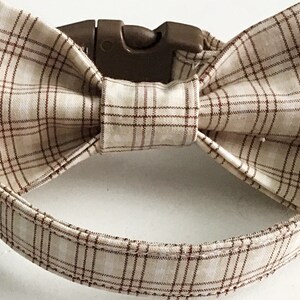 May include: A brown and beige plaid dog collar with a matching bow tie. The collar has a plastic buckle closure.