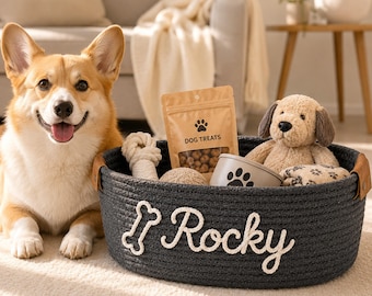 May include: A dark gray round rope storage basket with tan leather side handles. The basket features the white stitched text "Rocky" and a bone icon. Inside are a tan bag labeled "DOG TREATS", a plush dog toy, and a rope toy.