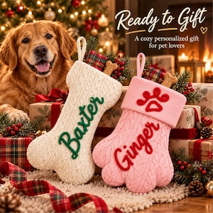 May include: Two knit Christmas stockings shaped like a bone and a paw print. The bone-shaped stocking is cream with the green embroidered name Baxter. The paw-shaped stocking is pink with the red embroidered name Ginger and a paw icon.