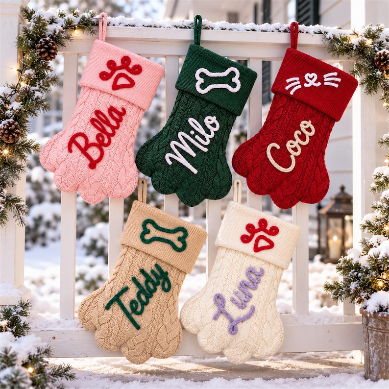 May include: Five paw-shaped knit Christmas stockings in pink, green, red, tan, and cream. Each stocking features a cuff with an embroidered icon and a name: Bella with a paw print, Milo with a bone, Coco with whiskers, Teddy with a bone, and Luna with a paw.